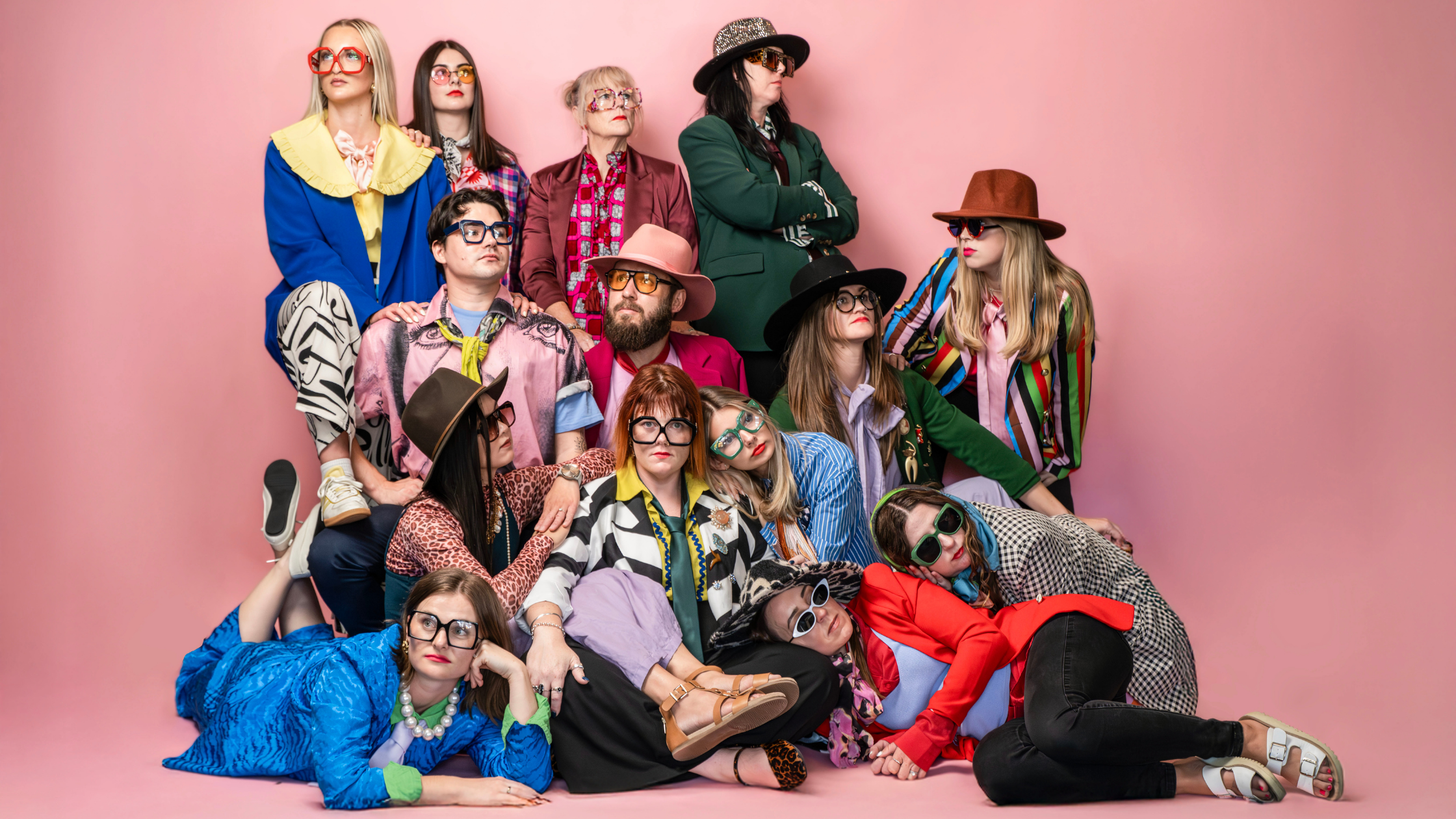 In front of a pink backdrop, the 14-strong Idyllic team crowds together, wearing bold colours, eccentric accessories, and inspired facial expressions.